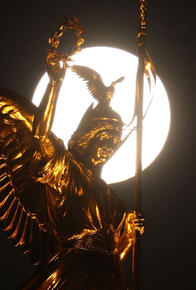 The statue of Victoria on top of the Victory Column in Berlin, Germany, is seen with the pink supermoon behind it