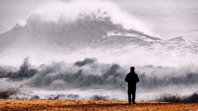 Homem olhando para ondas enormes em Nazaré
