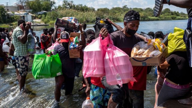 Migrantes con suministros cruzando el río.