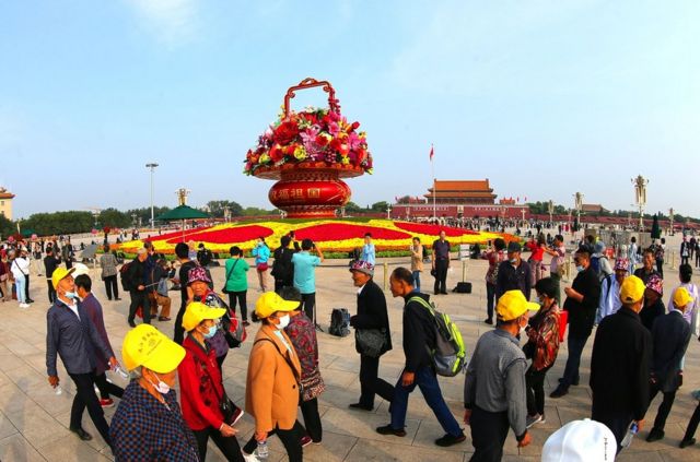 游客在北京天安门广场上的巨型花篮前拍照。