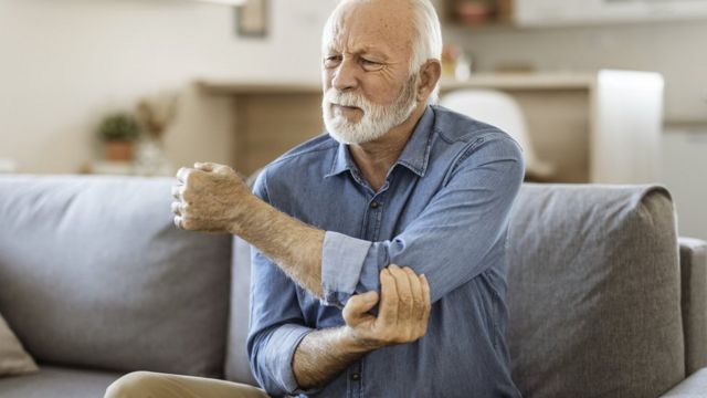 Um homem idoso segurando o cotovoelo com cara de dor