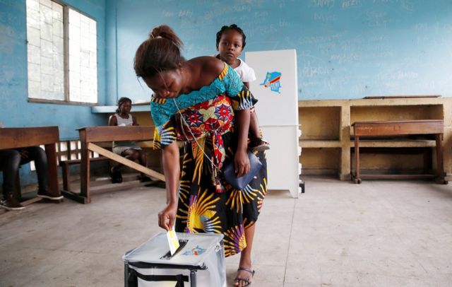 Woman casting her vote with a baby on her back.