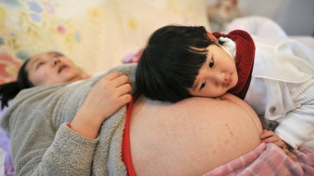 A woman, pregnant with her second child, lies on a bed as her daughter places her head on her mother's stomach in Hefei, Anhui province, China, in February 2014