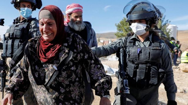 A Palestinian woman, accompanied by Israeli forces, reacts as a building is demolished in Yatta, in the Israeli-occupied West Bank (12 January 2022)