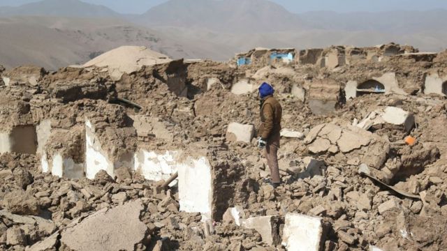 A man stands amidst collapsed homes