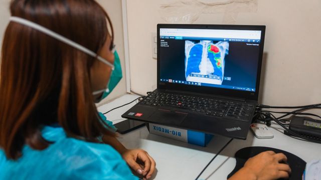 Uma profissional de saúde examina um raio-X no computador na clínica de Socios en Salud
