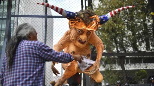 متظاهر يشعل النار في تمثال لترامب وعلى رأسه علم امريكا