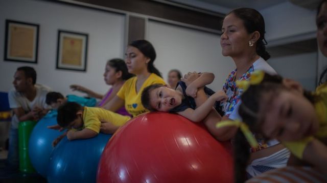 Em sala, famílias brincam com crianças com microcefalia usando bolas