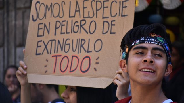 Jóvenes en México con una pancarta que dice "somos la especie en peligro de extinguirlo todo".