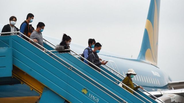 People wearing masks disembark from a plane