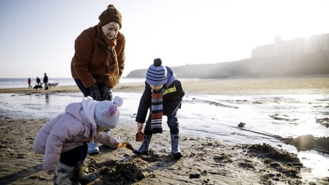 Abuela jugando en la playa con sus dos nietos pequeños.