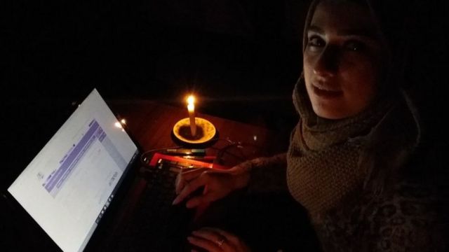 Mariam estudiando con su computadora a la luz de una vela