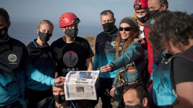 Flamini rodeada de su equipo sostiene un artículo de periódico al salir de una cueva.