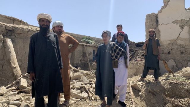 Image shows boys and men standing atop rubble