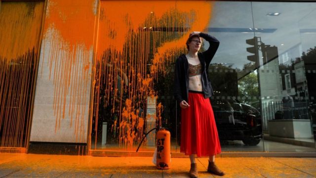 Женщина в длинной юбке на фоне залитой оранжевой краской витрины