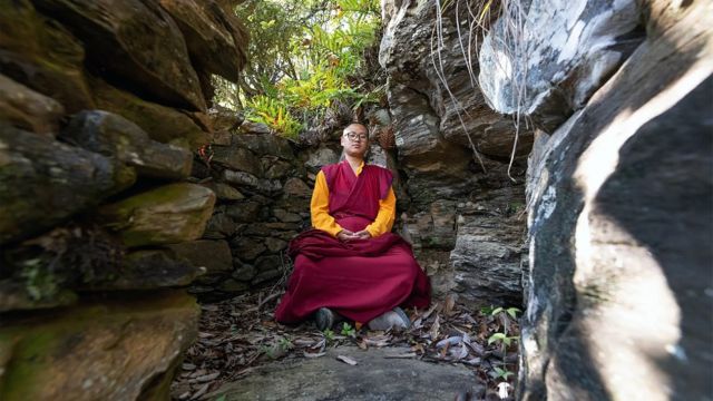 Rinpoche em um refúgio cercado por pedras no meio da floresta