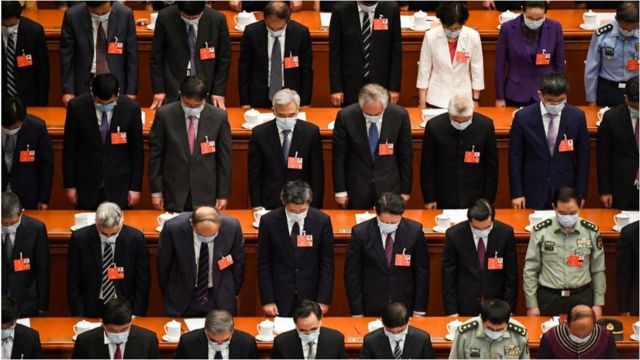 在政協會議開幕上上，戴著口罩的參會人員向新冠病毒病逝患者默哀。