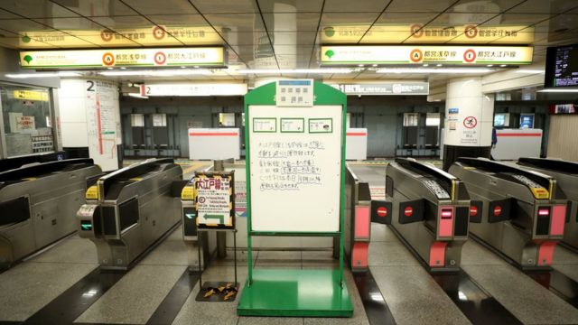 A deserted subway station in Tokyo, with a message board in front of the barriers