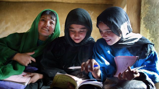 Tres adolescentes sonríen mientras miran sus libros en un colegio en Afganistán