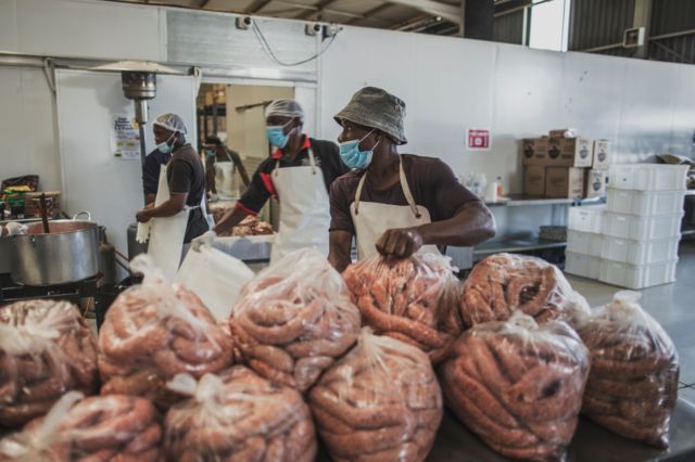 Men in a kitchen in Johannesburg prepare large bags full of uncooked sausages.