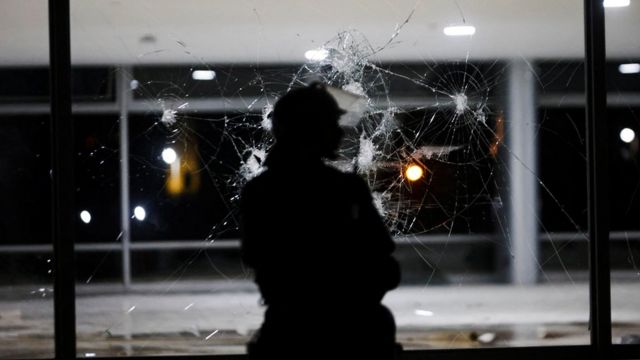 Sombra de policial diante de vidraça estourada