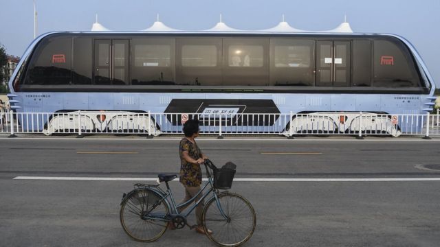 Una mujer maneja bicicleta mientras, al otro lado de la vía, circula el primer TEB en período de prueba