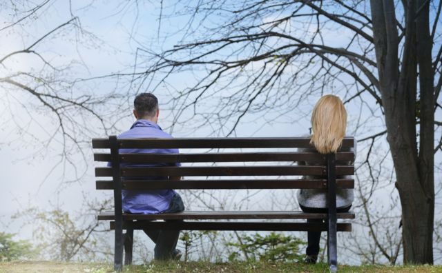 man and woman sitting far apart on a bench