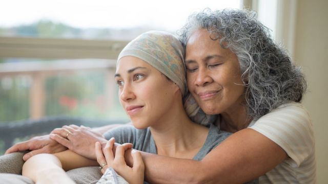 Mulher de 50 anos abraçando sua filha de 20 anos em tratamento contra o câncer