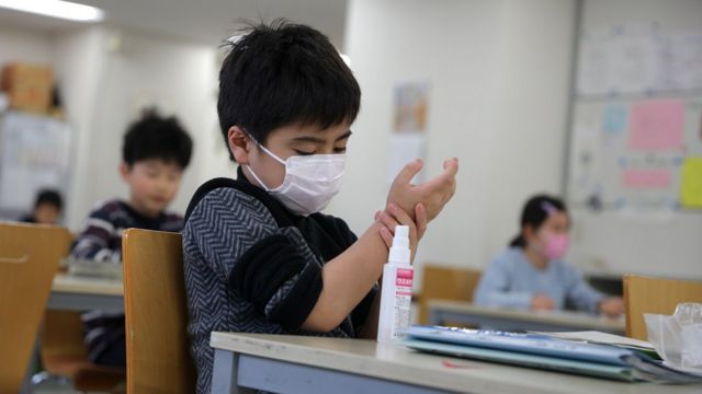 A child wears a protective face mask and applies hand sanitiser at a school in Japan