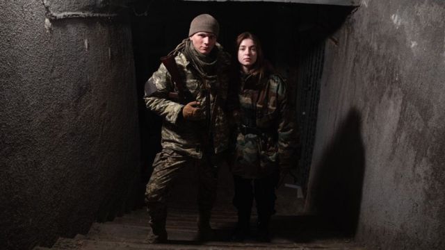 Svyatoslav Fursin et Yaryna Arieva en uniformes militaires tenant des armes.