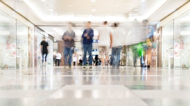 Vultos de pessoas caminhando em corredor de shopping