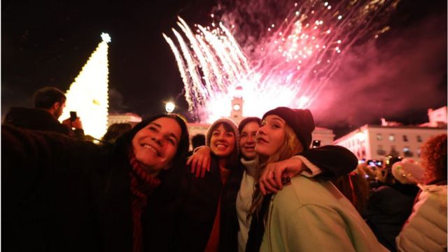 Cuatro mujeres se toman una selfie con fuegos artificiales de fondo en la Real Casa de Correos después de las Campanadas de Nochevieja, en la Puerta del Sol de Madrid.