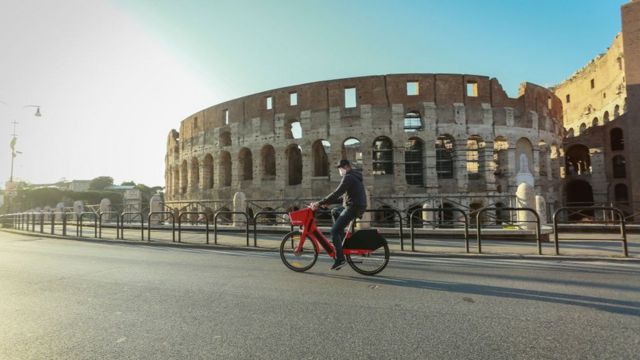 Un hombre con mascarilla circula en bicicleta frente al Coliseo en Roma, Italia.