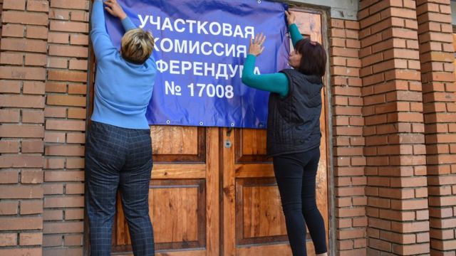 Des membres de la "commission électorale" accrochent une banderole dans un bureau de vote à Donetsk