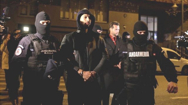 Andrew Tate e Tristan Tate são escoltados por policiais do lado de fora da sede da Diretoria de Investigação do Crime Organizado e Terrorismo em Bucareste (DIICOT)