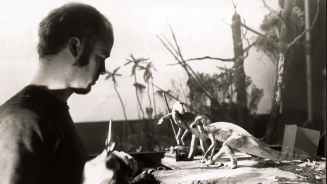Foto em preto e branco de um homem trabalhando com bonecos de dinossauros