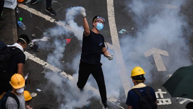 A protester throws back a tear gas during clashes with police outside the government headquarters in Hong Kong on June 12, 2019