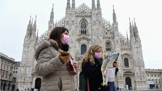 Two tourists wearing respiratory masks walk while holding a tourist map in Piazza Duomo in Milan, on March 5. 2020