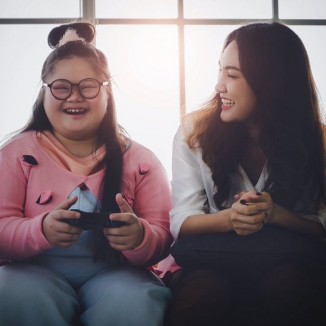 Young Down Syndrome woman playing videogames with her older sister