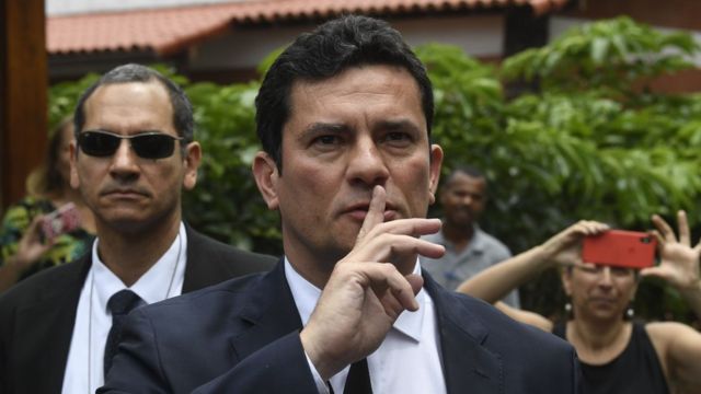 Juiz Sergio Moro faz sinal de silêncio, com o dedo indicador erguido em frente à boca, ao chegar à residência de Bolsonaro, no Rio