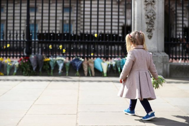 A little girl lays a bouquet of flowers outside Buckingham Palace