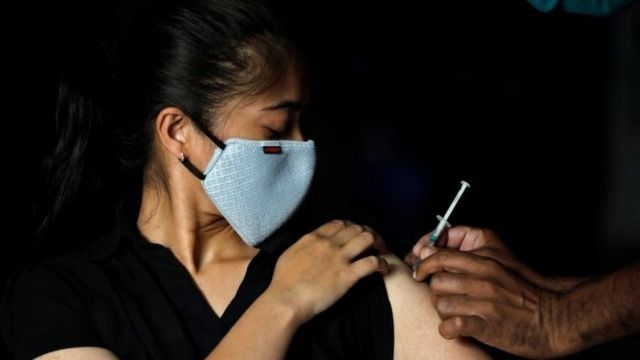 A woman reacts as she receives a dose of COVISHIELD coronavirus disease (COVID-19) vaccine manufactured by Serum Institute of India, at an auditorium that has been converted into a temporary vaccination centre in Ahmedabad, India, March 24, 2021.