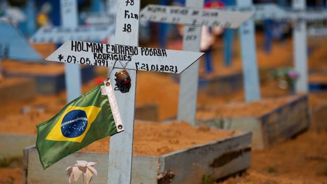 Foto de um cemitério, com uma cruz de madeira e uma bandeira do Brasil