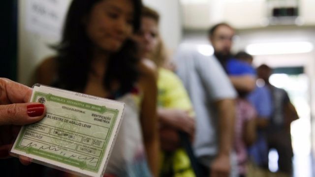 Mulher segura título de eleitor em frente a fila de votação em Brasília
