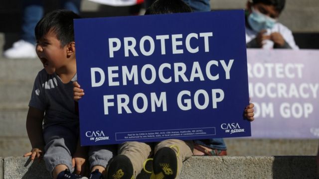 Personas con carteles que dicen: "protejan la democracia del Partido Republicano"