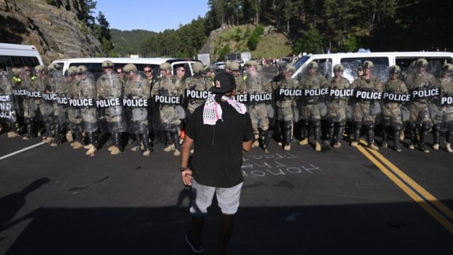 A man faces a row of police as activists and members of different tribes from the region block the road to Mount Rushmore National Monument in Keystone, South Dakota