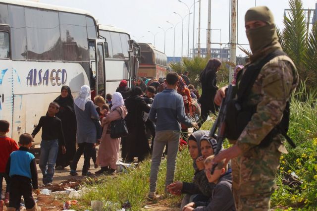 A rebel fighter stands near buses carrying people that were evacuated from the two villages of Kefraya and Foah, 15 April