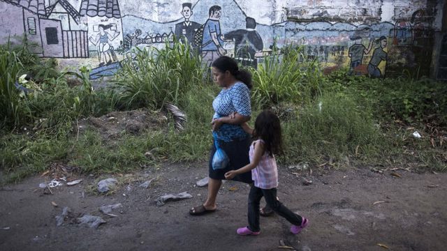 Mujer mayor pasea con una niña en un barrio de San Salvador.