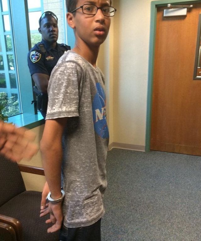 Ahmed Mohamed, 14, waits in handcuffs as a police officer looks on