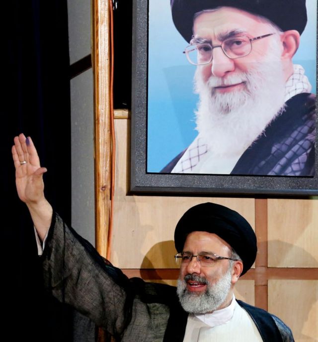 Utama di sebelah plakat Ayatollah Khamenei.